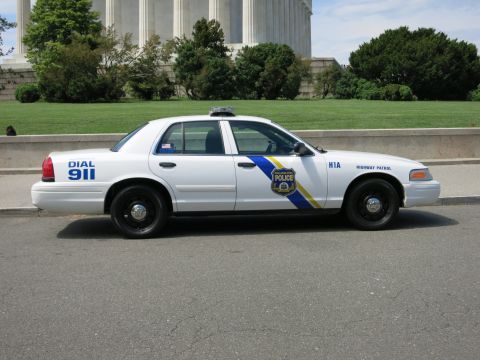 1991 Ford LTD Crown Victoria - Side profile of a white Philadelphia Police Highway Patrol Crown Victoria parked in front of a large marble monument, marked DIAL 911 and H…