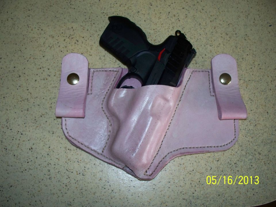 Pink leather IWB holster with brass snaps holding a black polymer pistol on a speckled counter