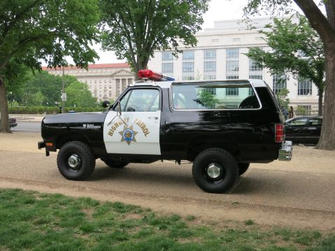 1991 Ford LTD Crown Victoria - lifted black-and-white Highway Patrol Dodge Ramcharger SUV on knobby tires, side profile with light bar and gold star, parked on a dirt pat…