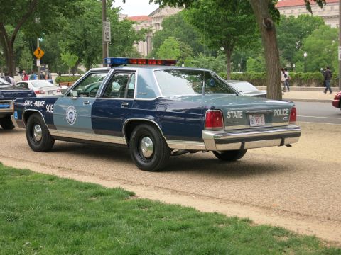 1991 Ford LTD Crown Victoria - Rear three-quarter view of a two-tone blue State Police Ford Crown Victoria marked STATE POLICE 90E with a red light bar, parked near a roa…