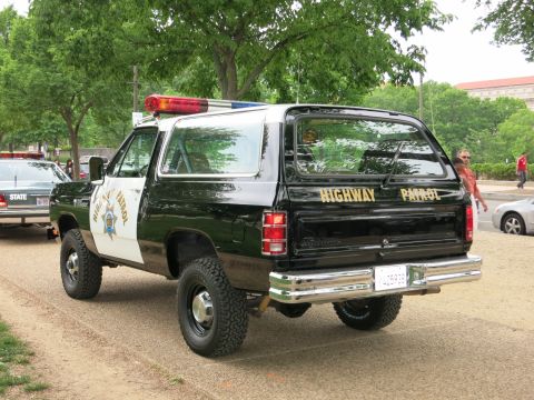 1991 Ford LTD Crown Victoria - Rear three-quarter view of a lifted black-and-white Highway Patrol Dodge Ramcharger SUV on knobby tires, marked HIGHWAY PATROL, parked on a…