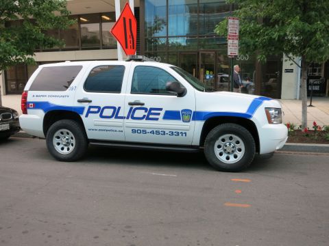 1991 Ford LTD Crown Victoria - white and blue Peel Police Chevrolet Tahoe SUV marked POLICE is parked at the curb in front of a glass office building downtown.