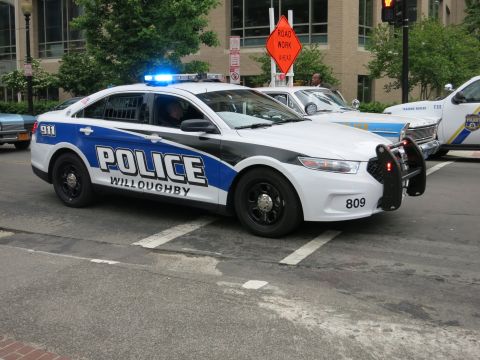 1991 Ford LTD Crown Victoria - white and blue Willoughby Police Ford Taurus Interceptor with activated emergency lights drives through a city intersection near a road wor…