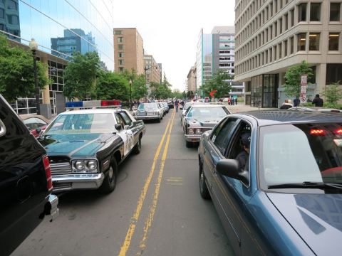 1991 Ford LTD Crown Victoria - vintage black-and-white police cruiser and other patrol cars sit in a long line down a downtown street between glass office towers.