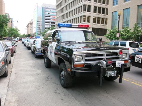 1991 Ford LTD Crown Victoria - black-and-white Dodge Ramcharger police SUV fitted with a front winch leads a line of patrol cars down an urban street.