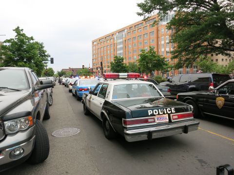 1991 Ford LTD Crown Victoria - black-and-white Chevrolet Caprice police car marked POLICE sits in traffic among other cruisers on a downtown street near a brick building.