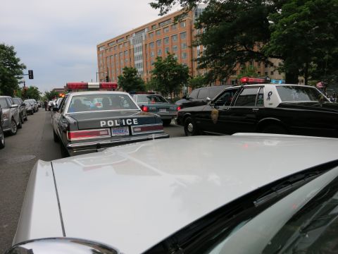 1991 Ford LTD Crown Victoria - Several black-and-white police cruisers, including one marked POLICE, are clustered in traffic on a downtown street with a brick building b…