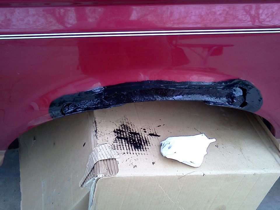 red vehicle's rear wheel well with black undercoating applied over a patch