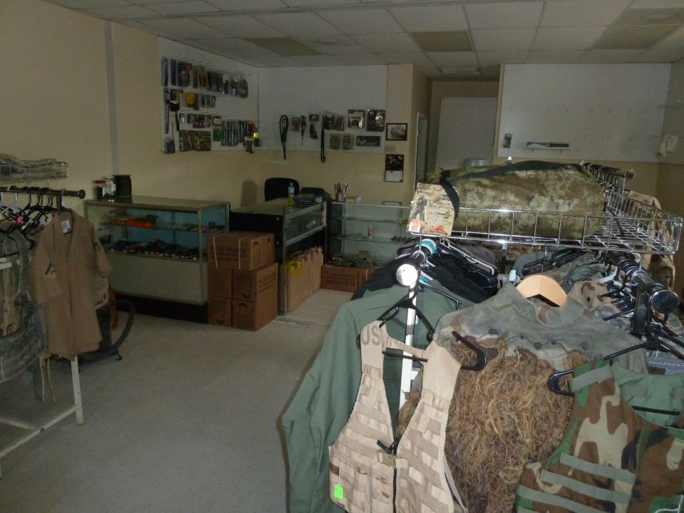 Interior of a store with racks of military clothing and gear, display cases, and shelves with items