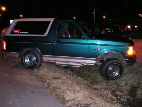 1996 Ford Bronco - Side view of a 1996 Ford Bronco parked outdoors at night, showing its dark green paint and tan trim.