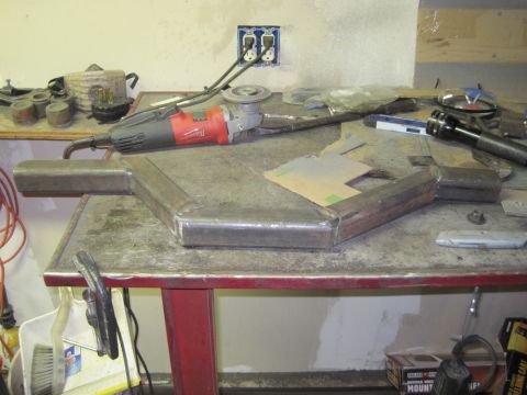 1989 Ford Bronco - A custom-welded metal part sits on a workbench next to an angle grinder and other tools.