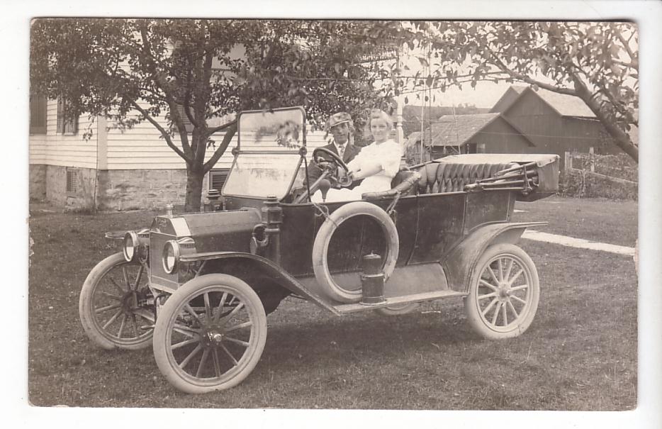 Black 1909 Ford Model T with a spare tire on the side, carrying two passengers