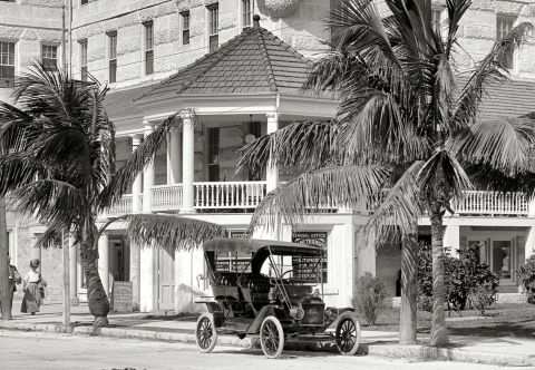 1909 Ford Model T - A vintage touring car is parked on a street in front of a building with a balcony and palm trees.