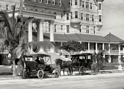 1909 Ford Model T - A 1909 Ford Model T is parked beside a horse-drawn carriage in front of a large building.
