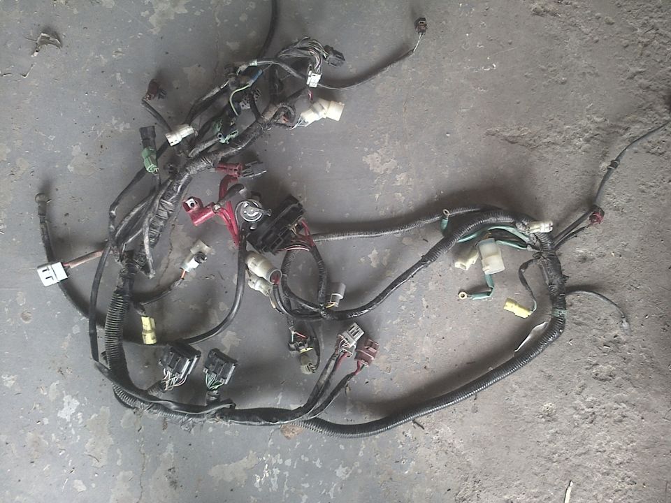 Wiring harness with multiple connectors and a fuse box, lying on a concrete floor