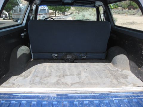 1988 Ford Bronco - The interior cargo area of a blue SUV is visible, with a folded rear seat and exposed wheel wells.