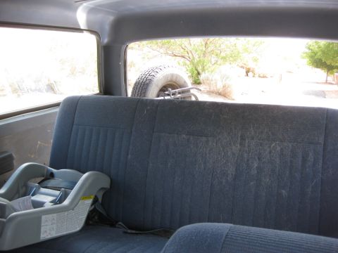 1988 Ford Bronco - The interior of a vehicle shows a rear seat with a child seat, and a spare tire is visible through the back window.