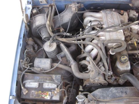 1988 Ford Bronco - Close-up of a Ford engine bay, the fuel injection system and battery, with visible "CAUTION" text on a fan shroud.