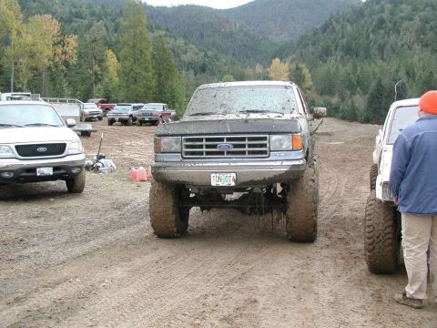 1988 Ford Bronco - Muddy 1988 Ford Bronco on a dirt track with other vehicles and trees in the background.