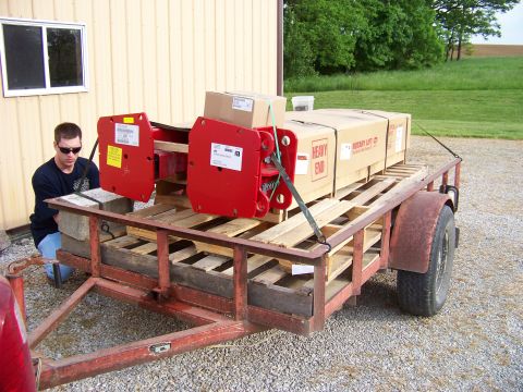 1995 Mercury Grand Marquis - A trailer carries red lifting equipment and boxed items, with a man securing the load. Text on the boxes indicates "HEAVY END" and "ROTARY…