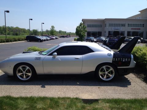 1988 Ford Bronco - A silver Dodge Challenger Daytona with a distinctive black rear wing is parked outside a dealership.
