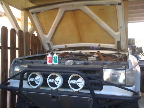 1990 Ford Bronco - A white SUV is parked with its hood open, revealing the engine bay and cleaning supplies on the fender.