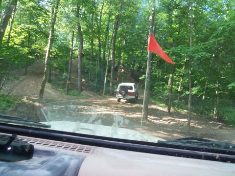 1989 Ford Bronco - A white 1989 Ford Bronco navigates a wooded trail, marked by a red flag.