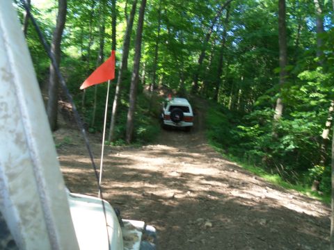 1989 Ford Bronco - Two vehicles navigate a dirt path through a dense forest during an off-road excursion.