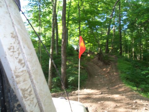 1989 Ford Bronco - An off-road vehicle's side is visible in the foreground, with an orange flag marking a dirt track ahead.