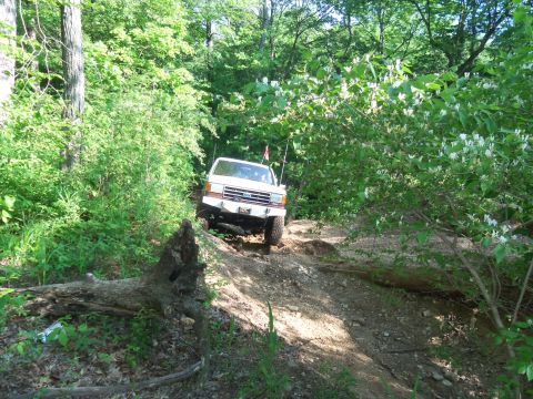 1989 Ford Bronco - White 1989 Ford Bronco navigates a challenging off-road trail through a dense forest.
