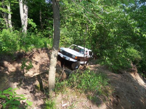 1989 Ford Bronco - A two-tone Ford Bronco navigates a steep, wooded trail.