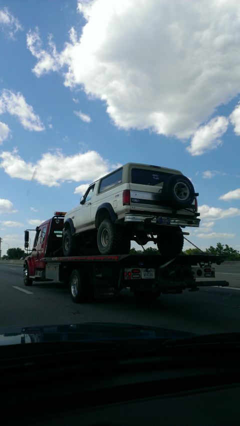 1995 Ford Bronco - A white 1995 Ford Bronco is transported on a tow truck under a cloudy sky.