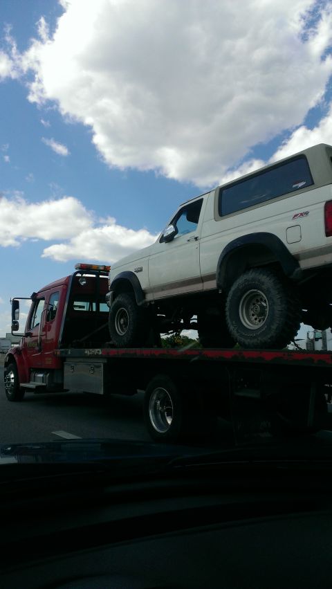 1995 Ford Bronco - A white 1995 Ford Bronco is loaded onto a red tow truck for transport.