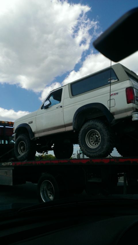1995 Ford Bronco - A white SUV is being transported on a flatbed truck under a cloudy sky.