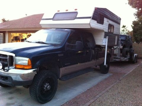 1987 Suzuki Samurai - A Ford F-Series truck is parked with a camper shell and a trailer carrying a Jeep.