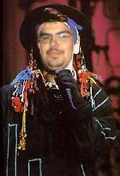 1991 Ford LTD Crown Victoria - A man dressed in a flamboyant outfit holds a microphone, with a website address visible at the bottom.