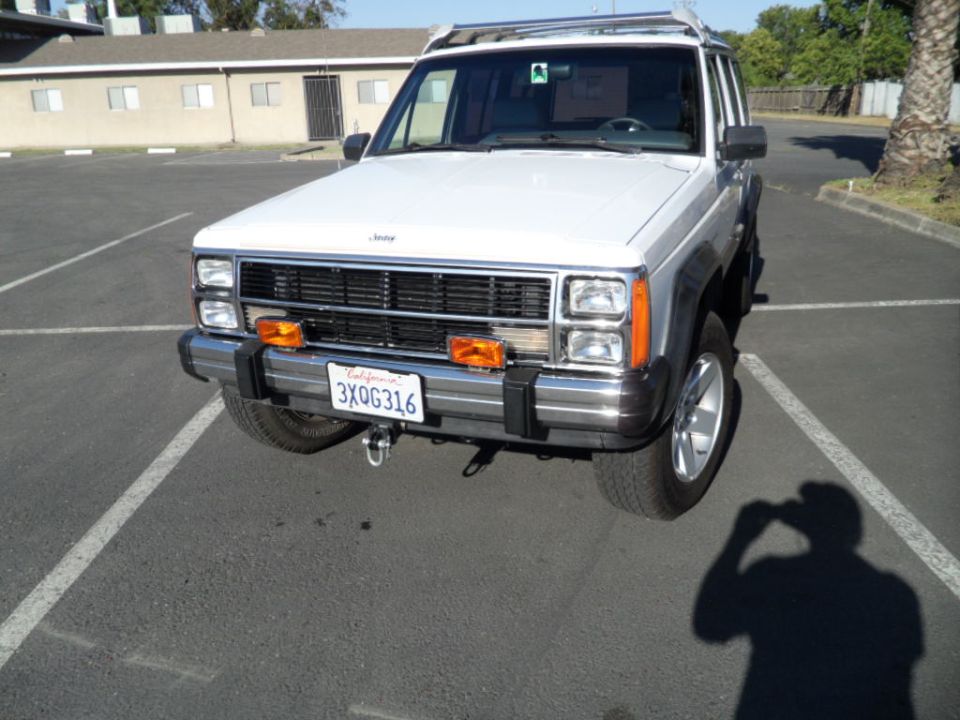 White Jeep Cherokee parked in a lot, front view. License plate is 3XOG316