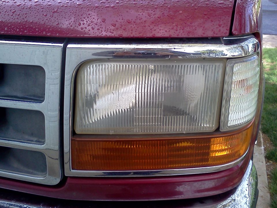 Close-up of driver-side headlight and amber turn signal on a rain-speckled burgundy Ford Bronco