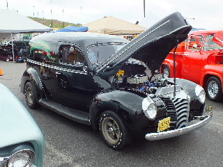 2013 Ford F-100 - Black sedan at car show with hood open, red truck visible behind it.