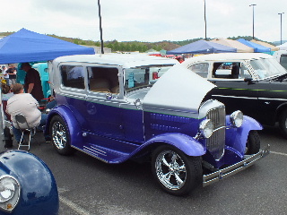 2013 Ford F-100 - A vintage sedan is displayed at an outdoor event with other vehicles and tents visible.