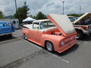 2013 Ford F-100 - A custom 1956 Ford F-100 pickup truck is displayed with its hood up at a car show, revealing the engine and custom modifications.