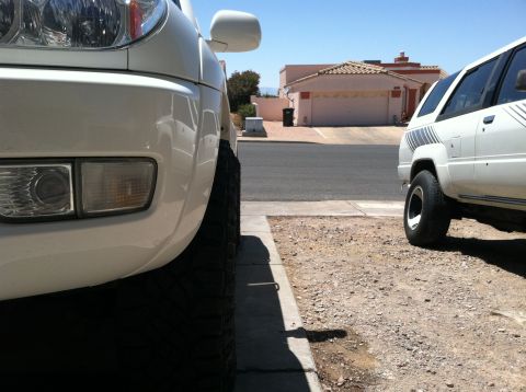 2003 Toyota 4Runner - Two white SUVs are parked on a street in front of houses. The closer vehicle is a Toyota 4Runner from the late 1980s.