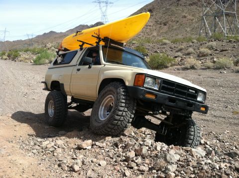 1985 Toyota Pickup/SR5 - This lifted 1985 Toyota Pickup SR5 is equipped with a kayak on its roof rack, navigating a , rocky terrain.