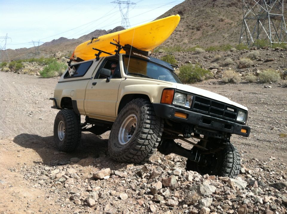 Tan 1985 Toyota Pickup SR5 with kayak on roof rack, off-roading