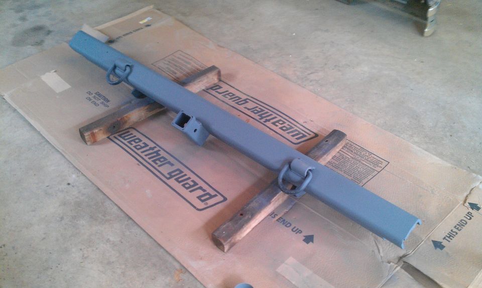 Painted steel rear bumper with D-ring recovery points and a 2-inch hitch receiver, resting on wooden blocks