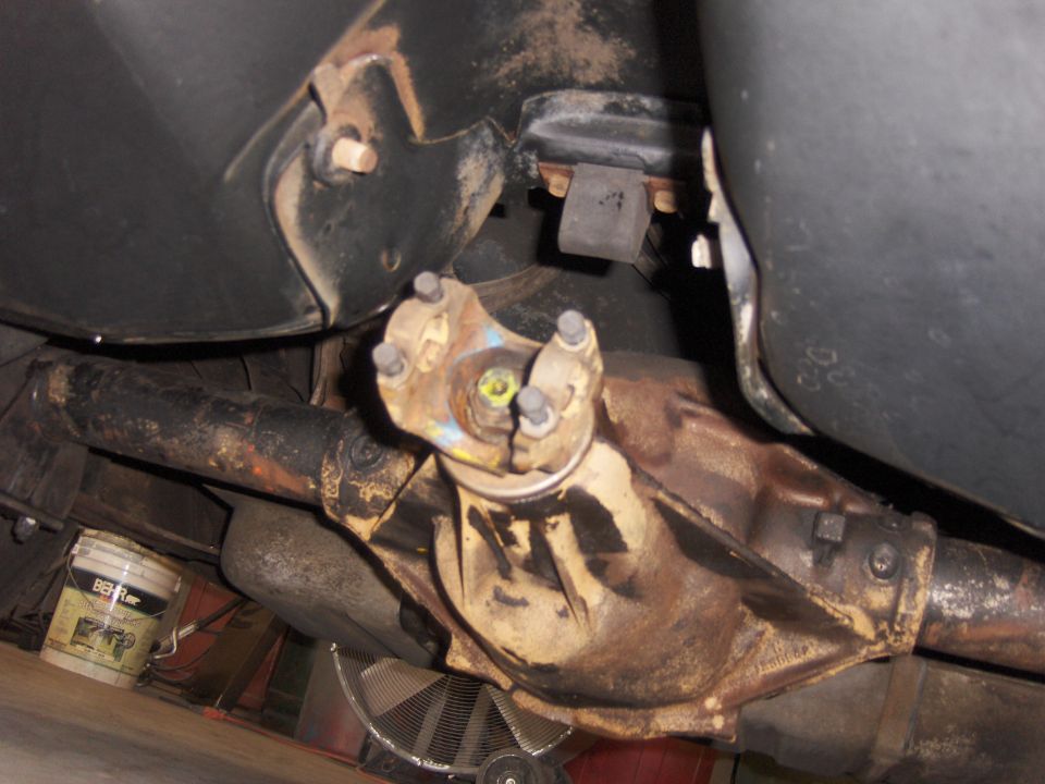 Underside view of a rusty rear differential and driveshaft assembly with a U-joint