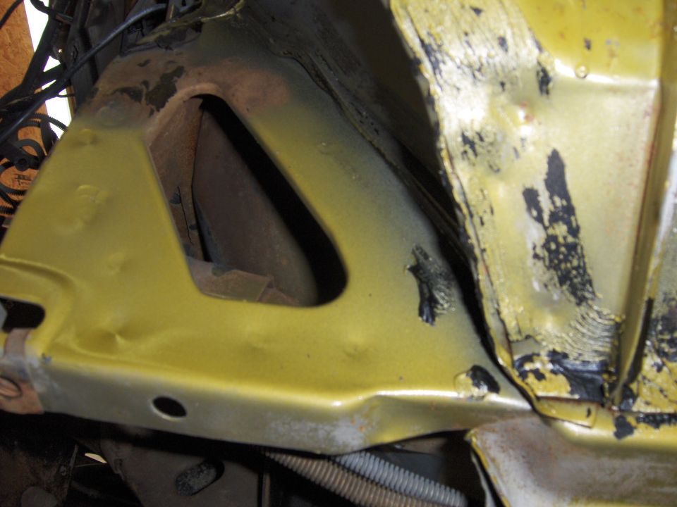 Close-up of a yellow car's engine bay, showing metal structure and some wiring