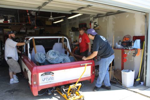 1968 Ford Bronco - People are working on a red and white pickup truck in a garage. The truck has a California license plate.