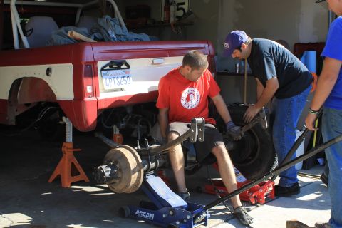 1968 Ford Bronco - Mechanics work on the rear suspension of a red and white 1968 Ford Bronco in a garage.