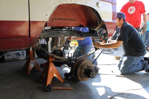 1968 Ford Bronco - Mechanics work on the suspension and drivetrain of a vehicle lifted on jack stands.